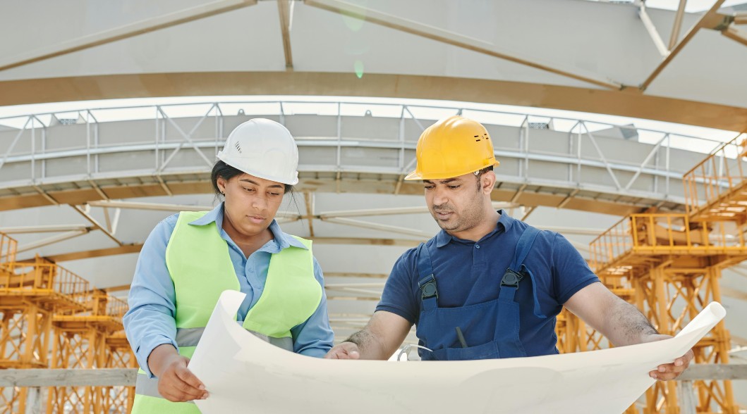 two people wearing hard hats reading blueprint two people wearing hard hats reading blueprint