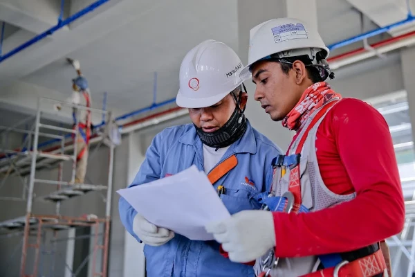 Two engineers in safety helmets reviewing construction plans at a worksite Two engineers in safety helmets reviewing construction plans at a worksite